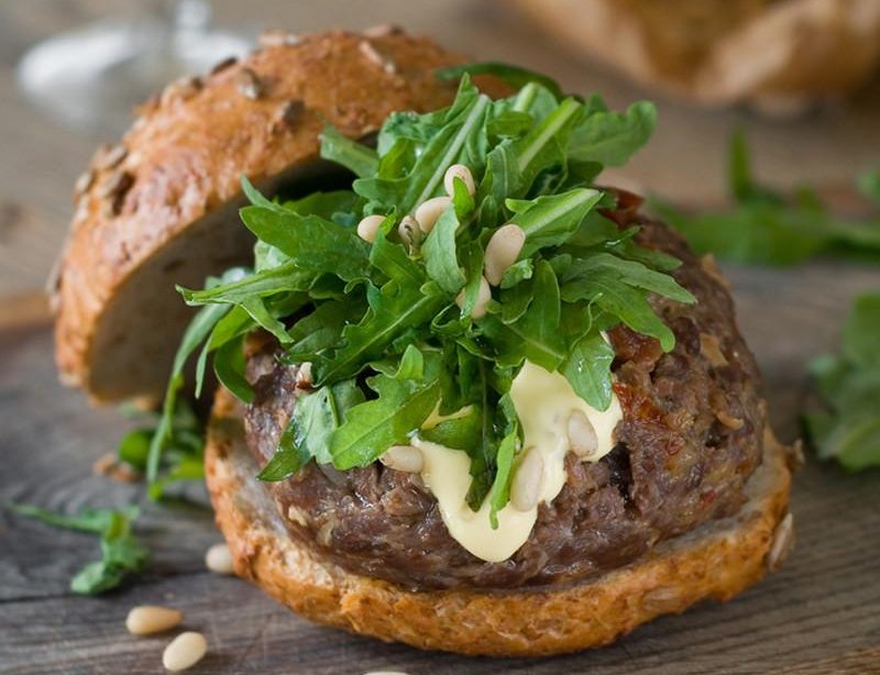 An alpaca burger is on a wooden table with lettuce on it.