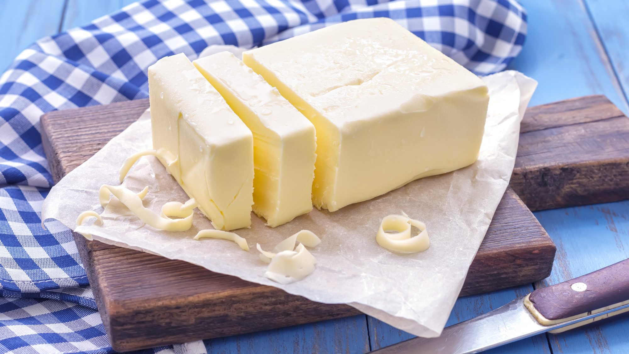 A block of butter sits on a wooden platter on a table. 