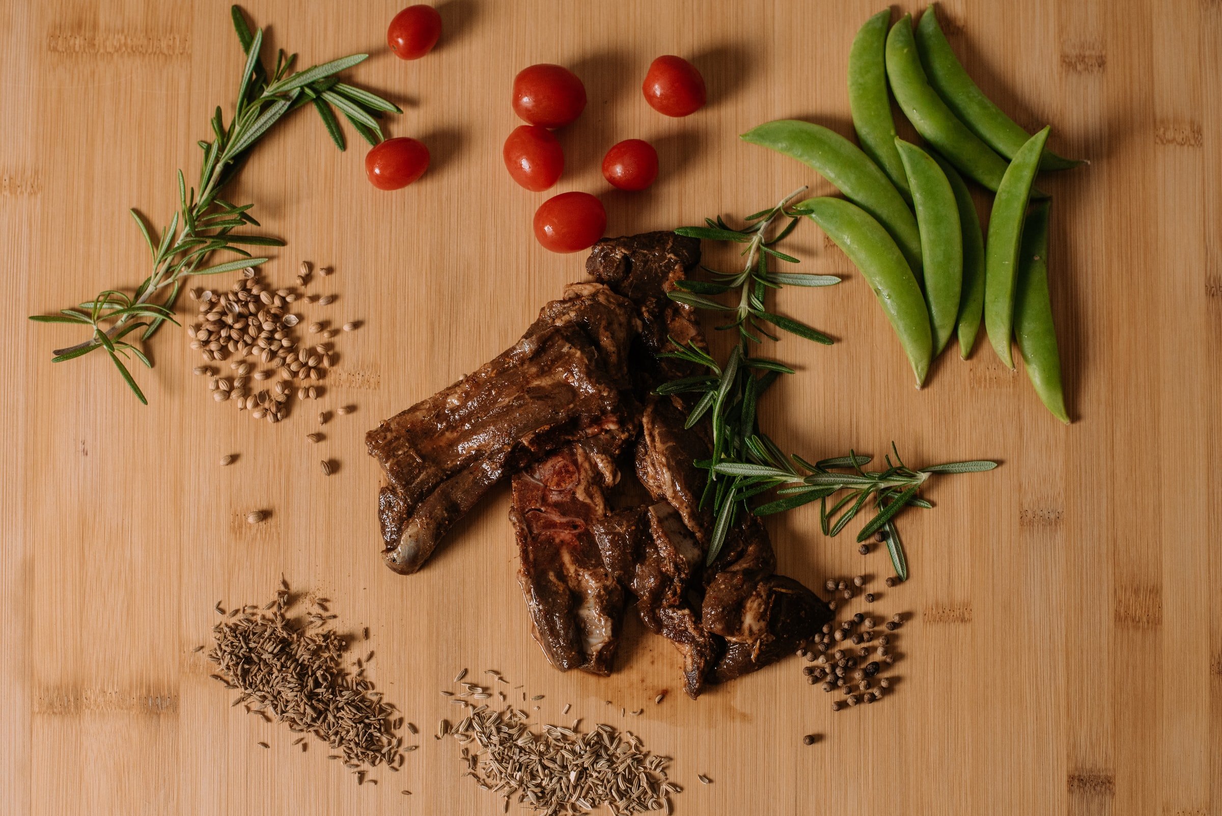 Goat meat is shown on a wooden counter with spices and vegetables surrounding it.