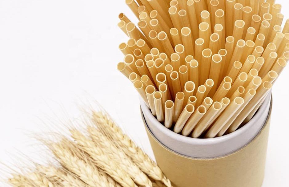A grouping of golden coloured straws are shown in a cup next to a wheat sheaf.