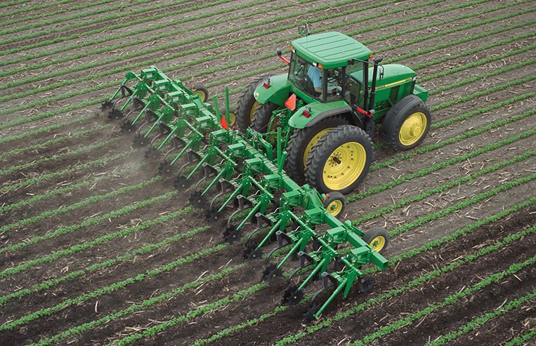 A tractor pulls a modern cultivator through a farm field.