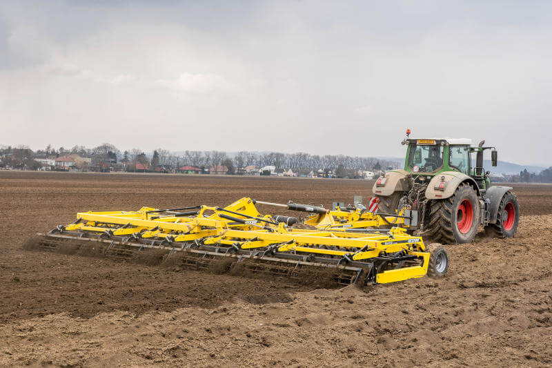 A tractor pulls a modern cultivator in a field.