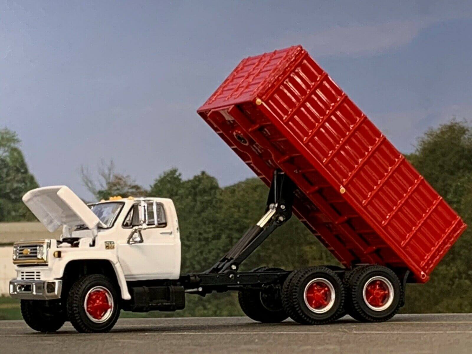 A grain truck has its box lifted up with an auger and grain bin in the background.