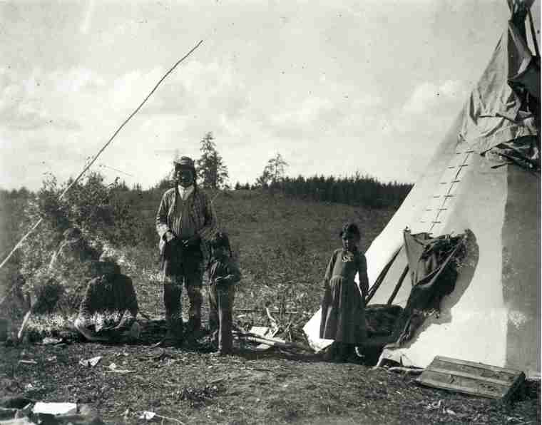 A photograph of a First Nations family in front of their tipi wearing western clothing. Taken in Prince Albert District, NWT in 1901.