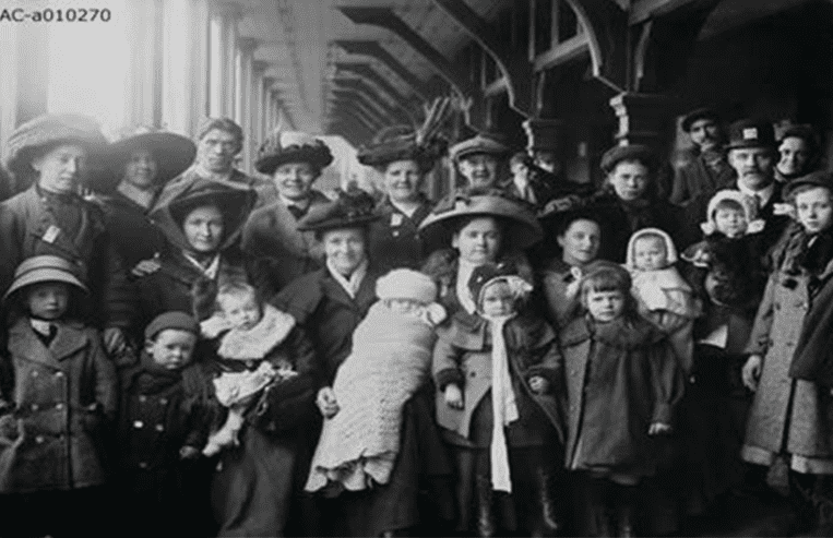 A group of settlers are standing in a line at a train station.