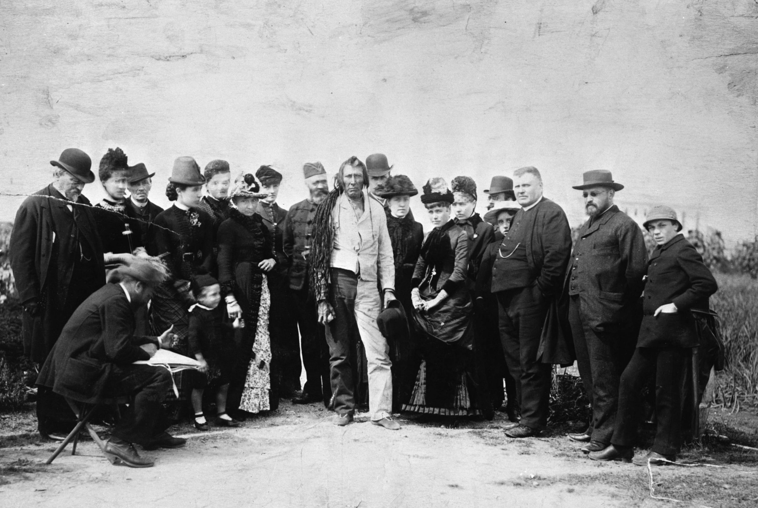 A First Nations man stands for a photo amongst a group of White men and women in formal wear.