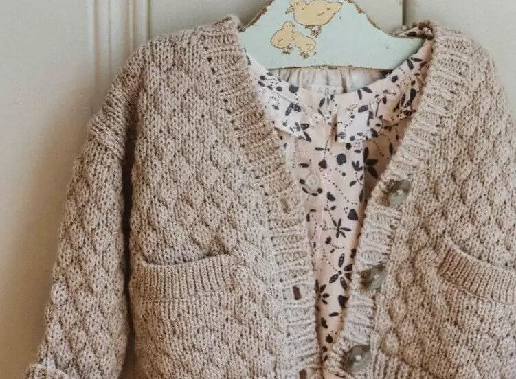 A sweater hangs on a hanger on a wooden wall background.