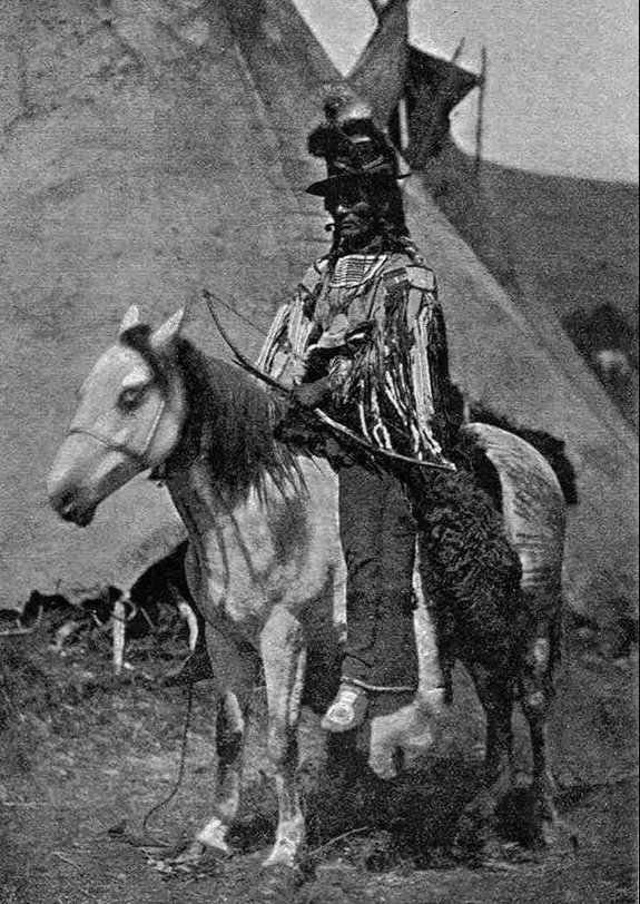 Chief Star Blanket on his horse, in front of two tipis.
