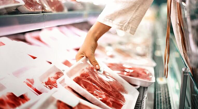 Buying meat at a supermarket. A woman reaches for a package of meat in the meat aisle of a grocery store.
