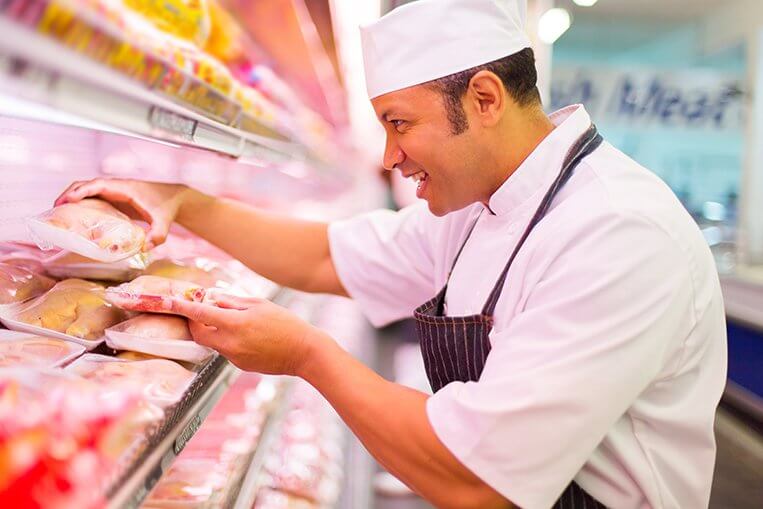 A butcher at a grocery store places packages of meat onto the shelves.